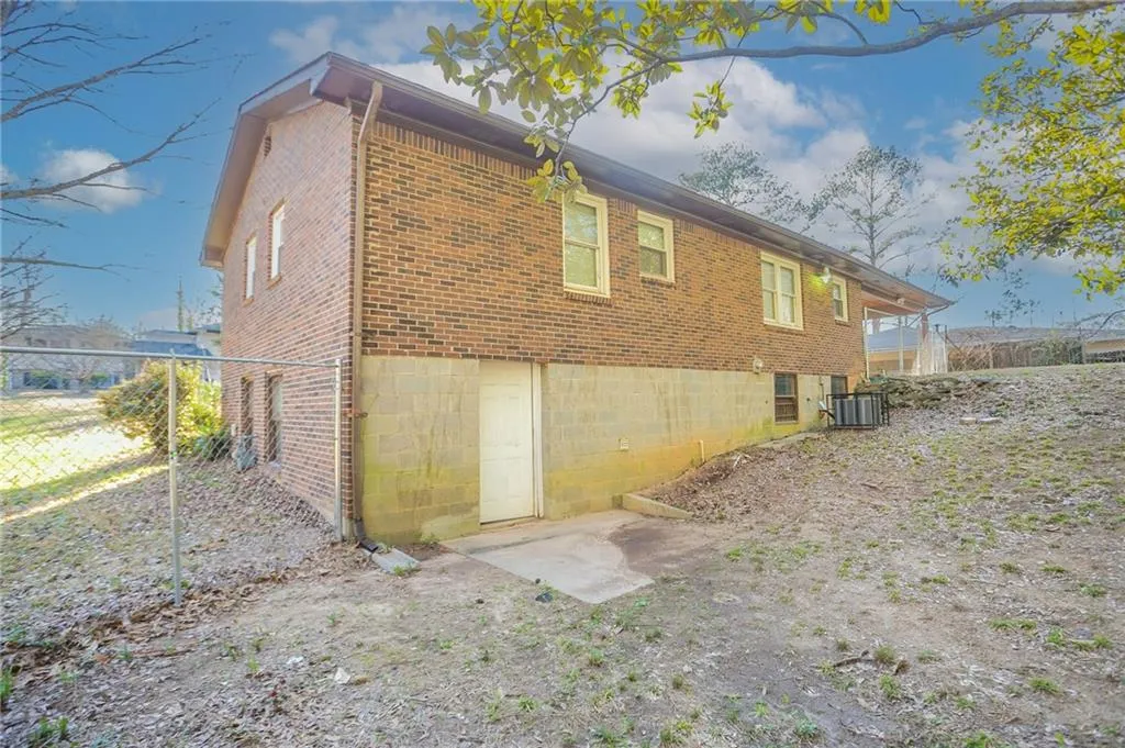 Back of property featuring central AC unit, fence, and brick siding