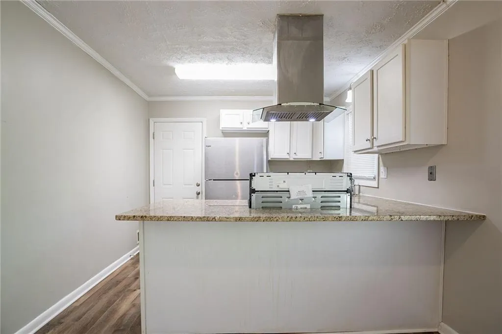 Kitchen with light stone counters, a peninsula, island exhaust hood, freestanding refrigerator, and a textured ceiling