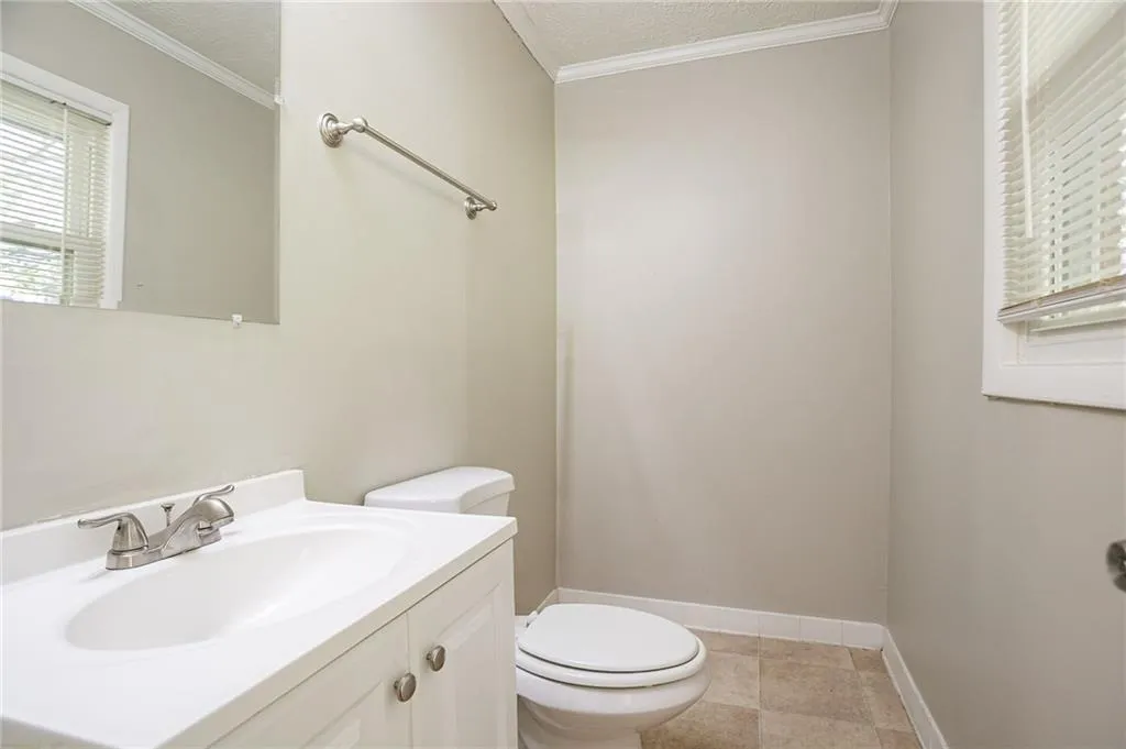 Bathroom with toilet, ornamental molding, a textured ceiling, baseboards, and vanity