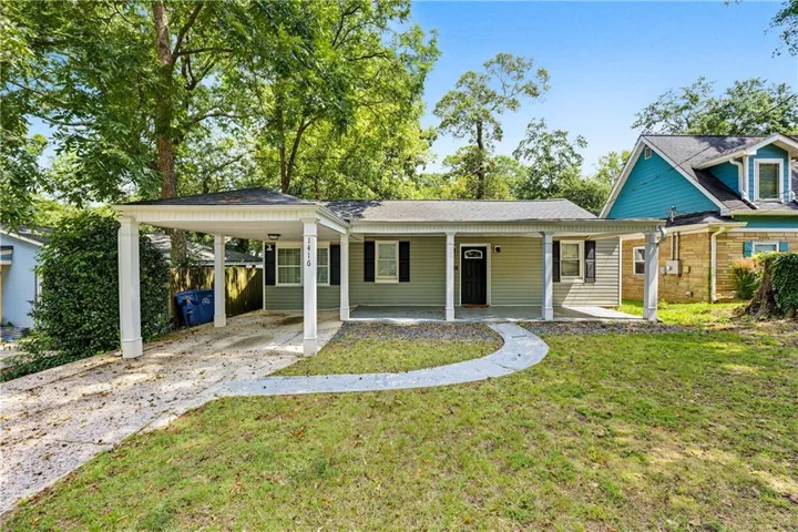 Single-story residence featuring light green siding, a covered porch, a covered carport, black front door, and a concrete pathway leading to the entrance