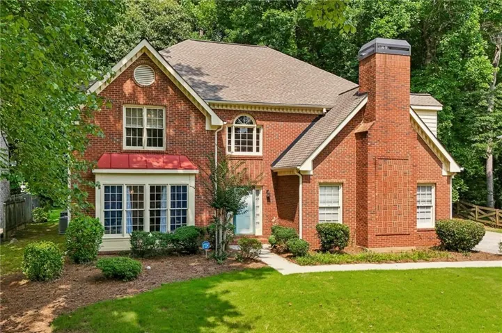 Brick Colonial estate featuring a two-story facade with arched transom windows, professional landscaping with mature foundation plantings, a brick chimney with decorative cap, and a manicured lawn framed by mature trees