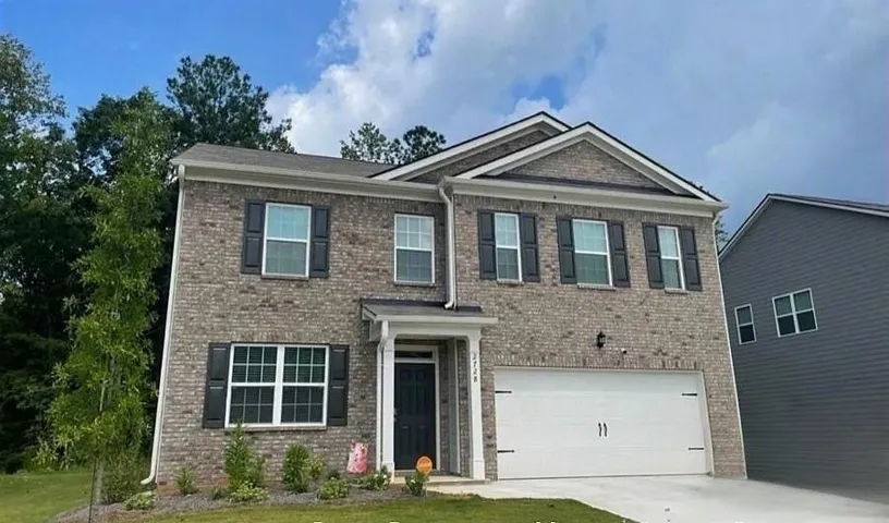 Two-story brick facade residence with black shutters, an integrated two-car garage, and a covered entry