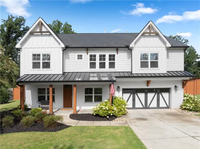 White exterior with board and batten siding, dark metal roofing accents, a prominent front entry with wood columns, and an integrated two-car garage