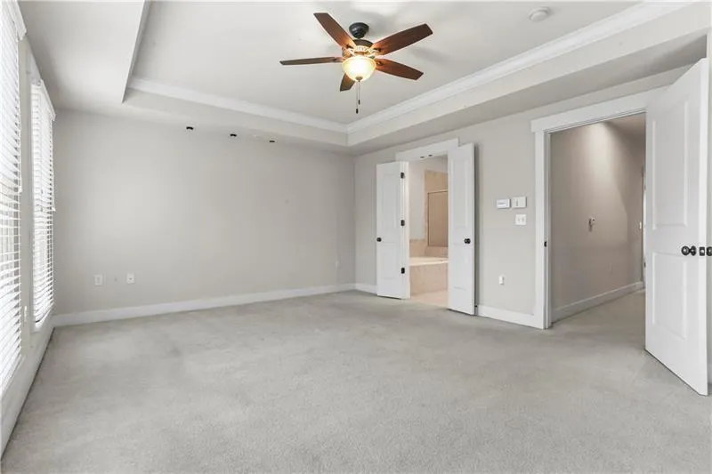 Unfurnished bedroom with ornamental molding, light colored carpet, a raised ceiling, baseboards, and ensuite bath