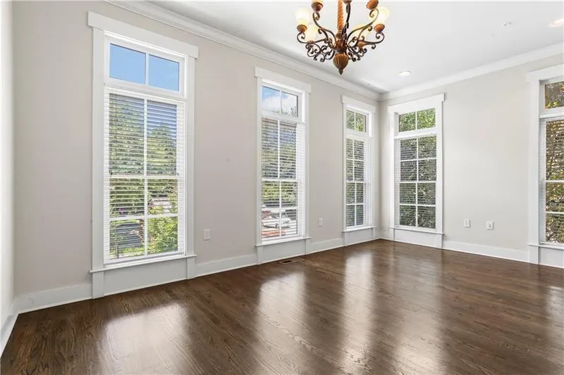 Empty room with a chandelier, crown molding, wood finished floors, and baseboards