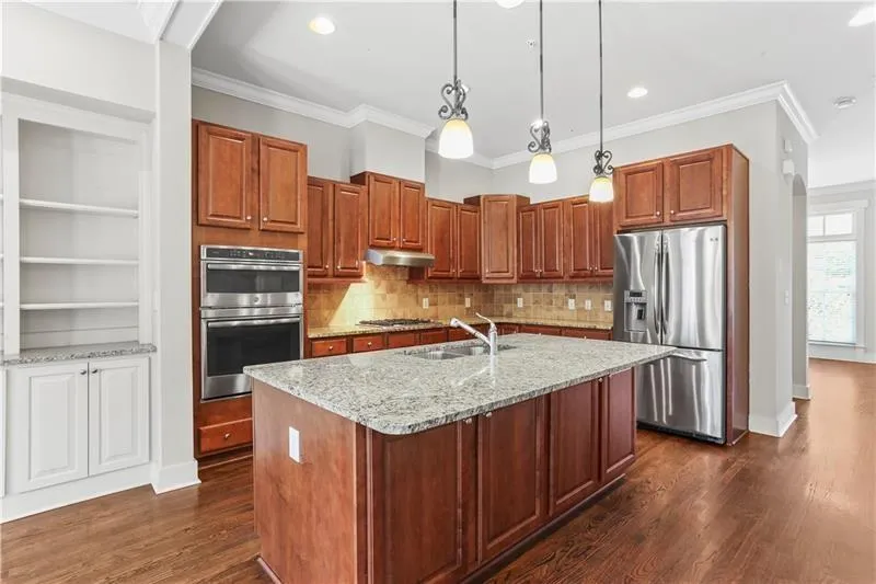 Kitchen with appliances with stainless steel finishes, under cabinet range hood, dark wood-style floors, backsplash, and light stone counters