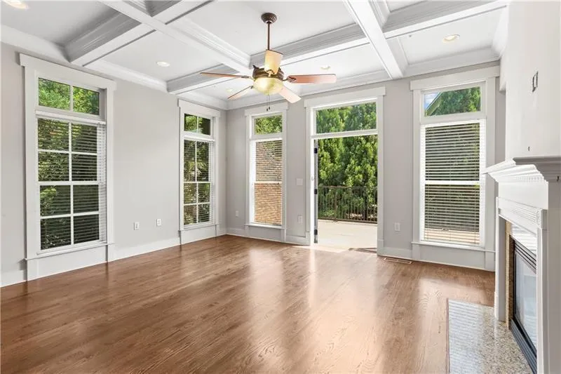 Unfurnished living room featuring a premium fireplace, coffered ceiling, a ceiling fan, wood finished floors, and beam ceiling