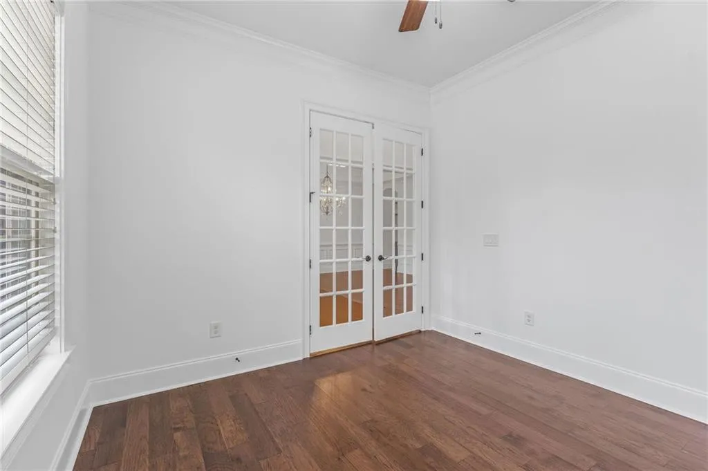 Office ornamental molding, dark wood-type flooring, ceiling fan, and french doors