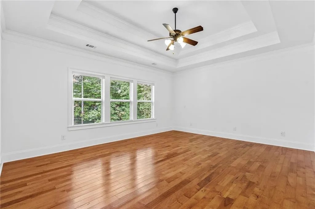 Primary with a tray ceiling, ceiling fan, hardwood / wood-style floors, and crown molding