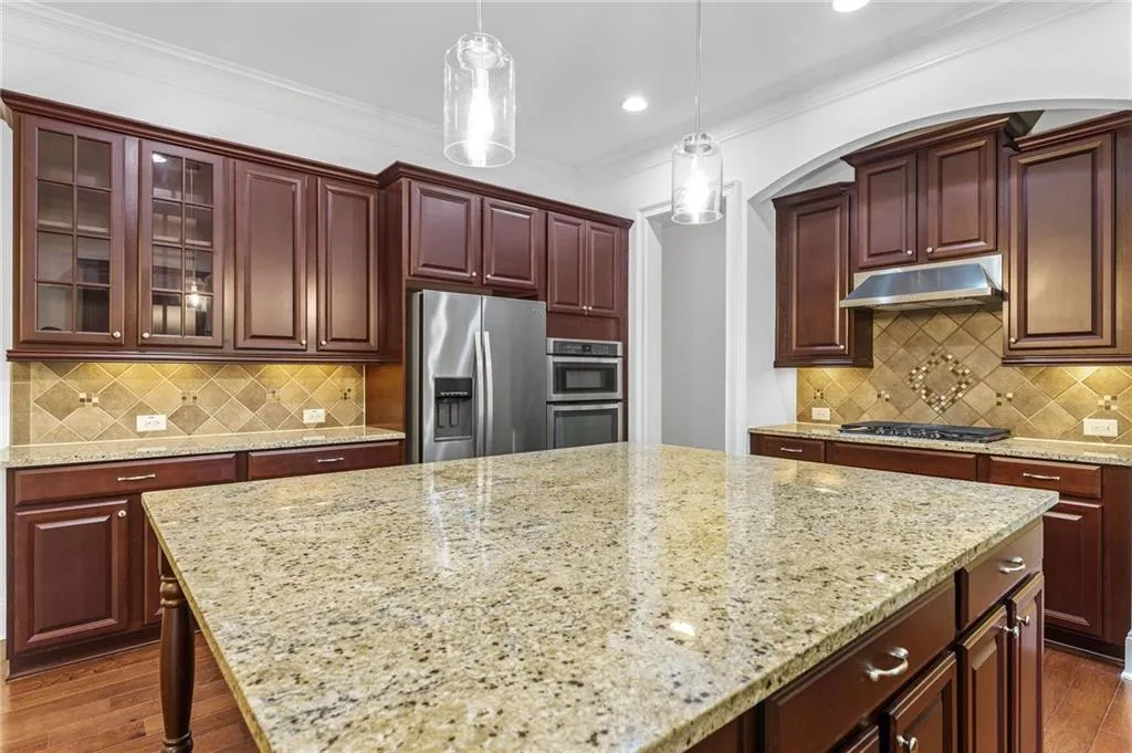 Kitchen with pendant lighting, dark hardwood / wood-style floors, decorative backsplash, stainless steel appliances, and crown molding