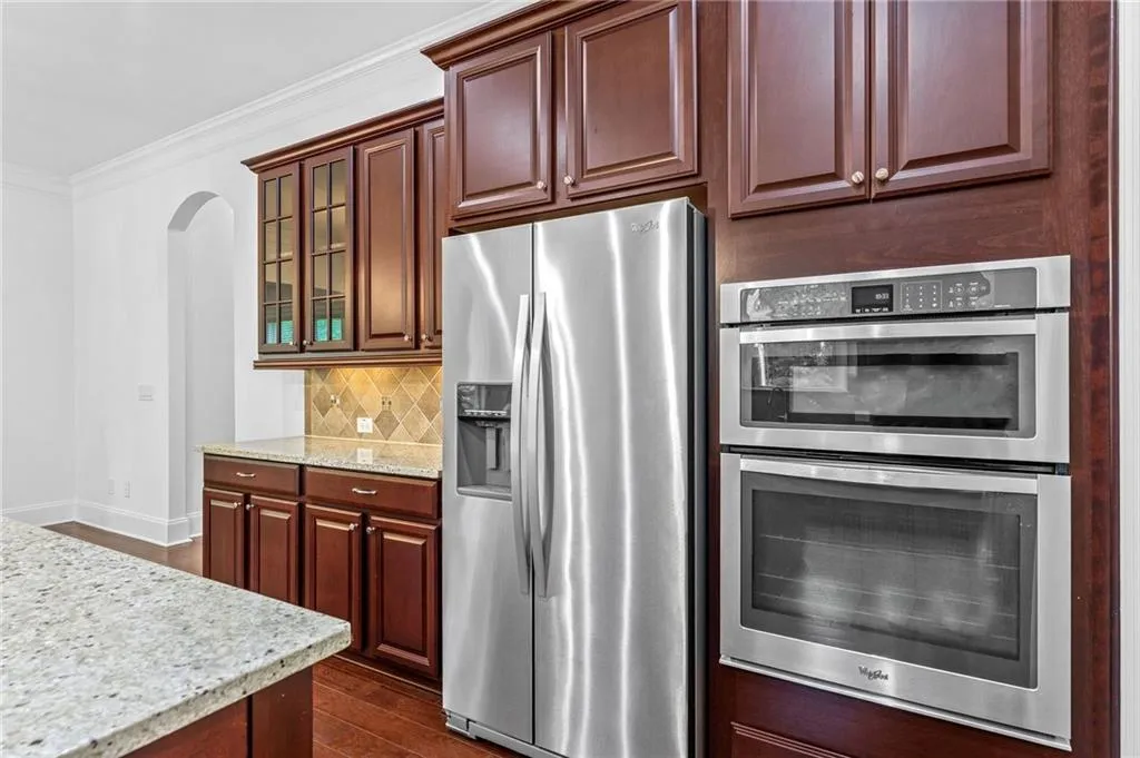 Kitchen with appliances with stainless steel finishes, decorative backsplash, dark wood-type flooring, light stone countertops, and crown molding