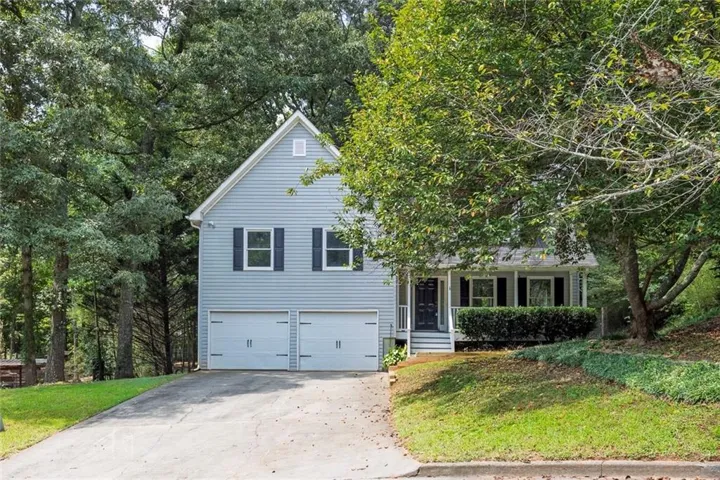 Front exterior view of the home featuring a newly rebuilt front entry steps, freshly trimmed mature tree, two-car garage, covered front porch, and wooded surroundings along a gently sloped driveway.