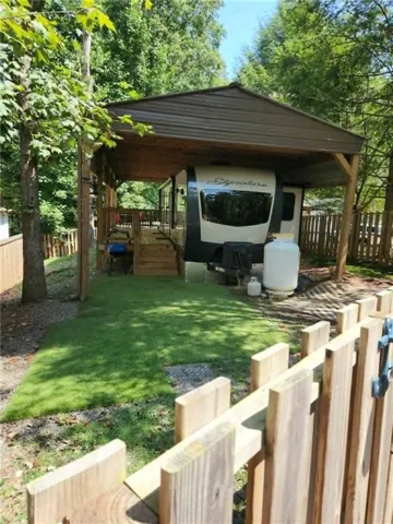 Canopied outdoor living area with a wood deck, wood privacy fence, and manicured lawn