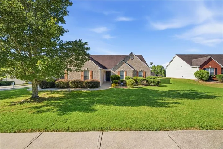 Brick exterior residence with a shingled roof, front landscaping, mature tree, and a concrete pathway