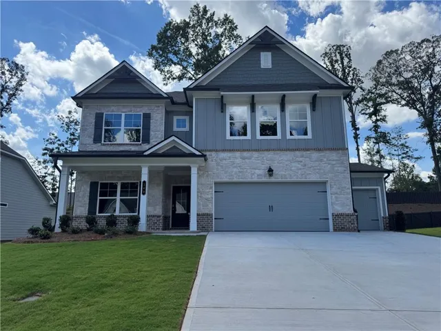 Two-story residence featuring a stone and siding exterior, an attached two-car garage, and a covered front porch with columns