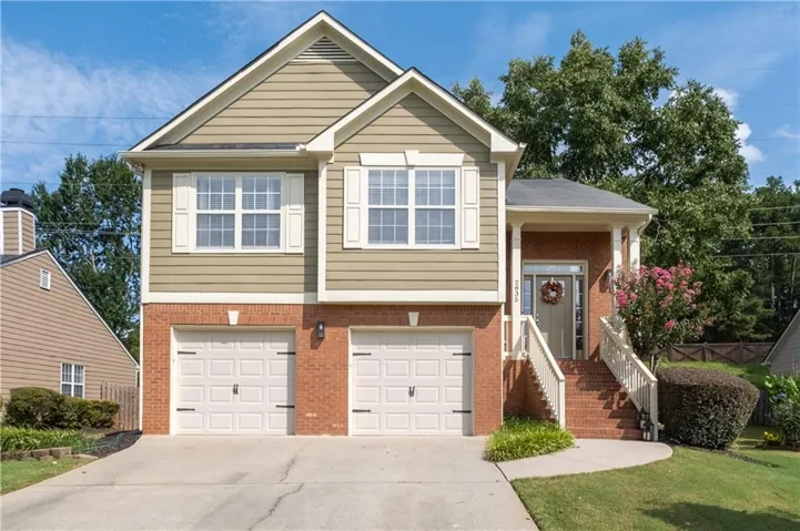 Two-car garage with almond colored panel doors, brick and freshly painted siding exterior, concrete driveway, front porch with columns, and mature landscaping