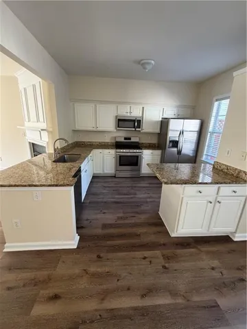 Well-appointed kitchen featuring white cabinetry, stainless steel appliances, wood-finish flooring, and light-toned countertops