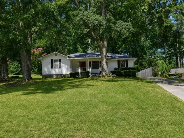 White-sided exterior with black shutters, covered front porch, concrete driveway, front yard with mature trees, and landscaping