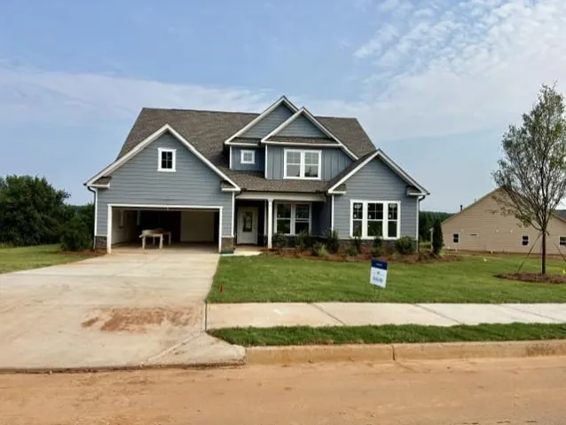 Blue siding exterior with stone accenting, prominent white trim, a covered porch entry, and a two-car garage
