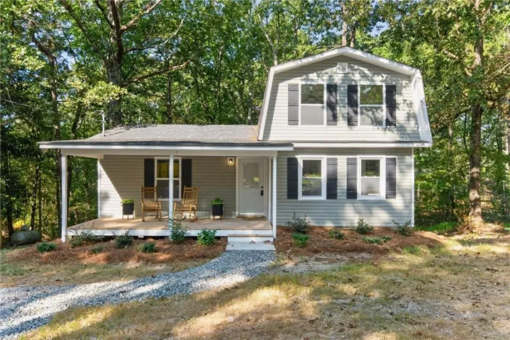 Two-story residence with light gray siding, dark shutters, a covered porch, and a gravel driveway