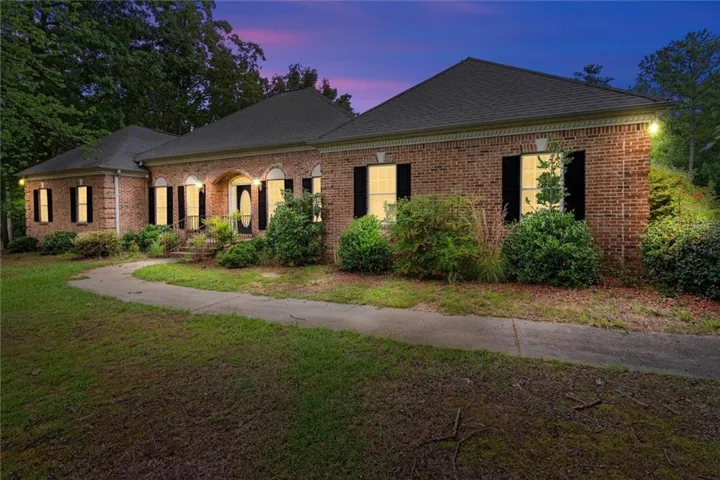 Brick exterior featuring arched window details, dark shutters, a covered entry, and established landscaping
