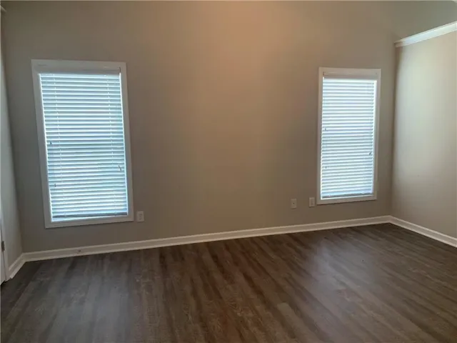 Wood-finish flooring with white trim, neutral wall paint, and two windows with blinds