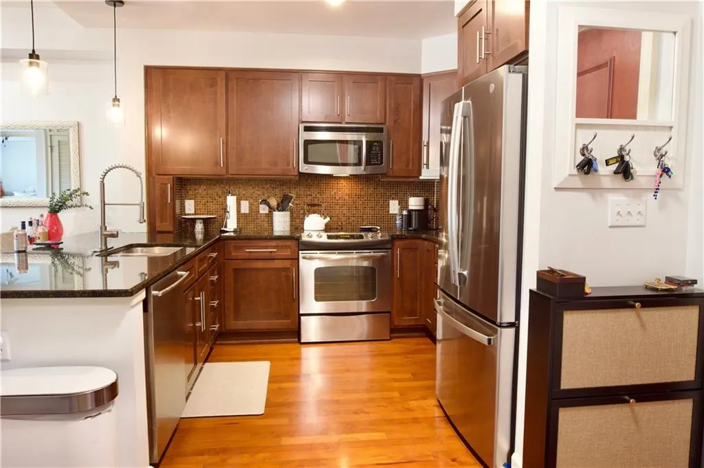 Kitchen featuring brown cabinetry, dark stone counters, stainless steel appliances, and light wood-style floors