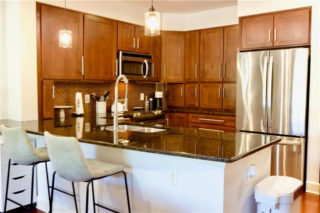 Kitchen with appliances with stainless steel finishes, brown cabinetry, dark stone counters, a peninsula, and pendant lighting