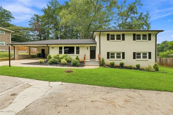 White painted brick exterior with dark shutters, established landscaping, and a covered carport