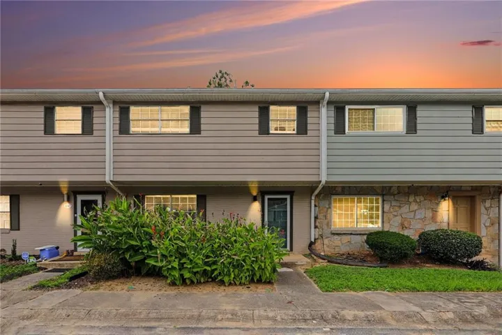 Two-story townhome with stone and siding facade, contrasting dark shutters, and front landscaping