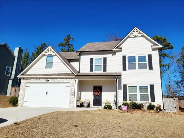 View of front of home with covered porch, driveway, a garage, stone siding, and a shingled roof