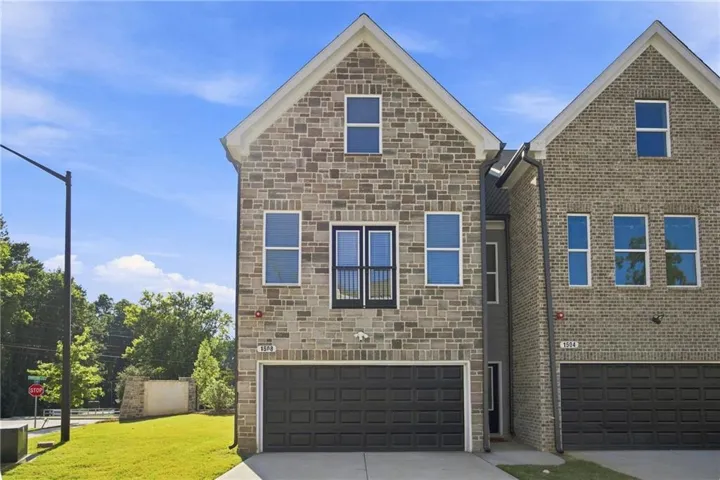 Stone-clad exterior, multi-pane windows, black garage door, and a Juliette balcony