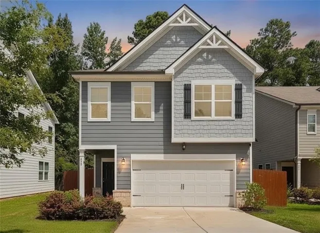 Two-story residence featuring a gray siding and shingle exterior, a white paneled garage door, and a covered entry