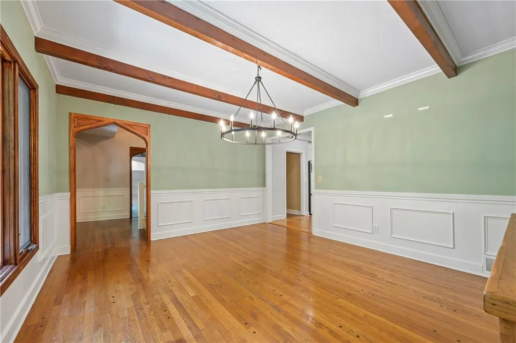 Unfurnished dining area with hardwood / wood-style flooring, crown molding, a chandelier, a wainscoted wall, and arched walkways