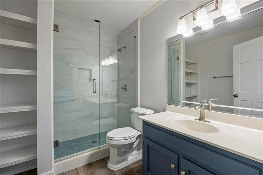 Full bath featuring a shower stall, vanity, dark wood finished floors, crown molding, and a spacious closet