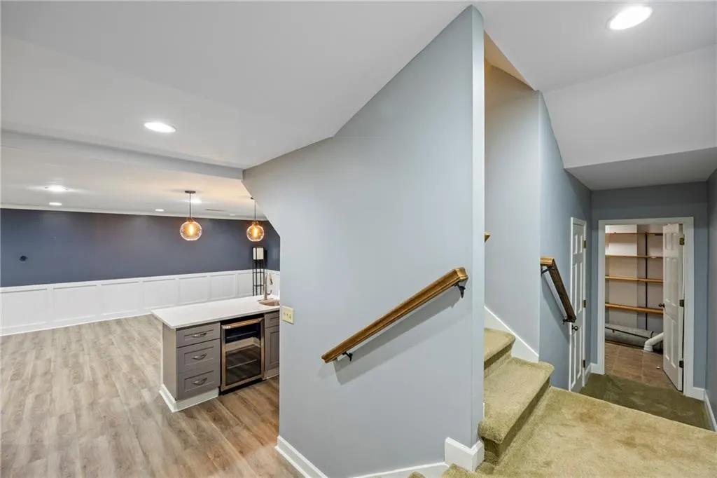Indoor wet bar with recessed lighting, light countertops, wine cooler, hanging light fixtures, and wainscoting