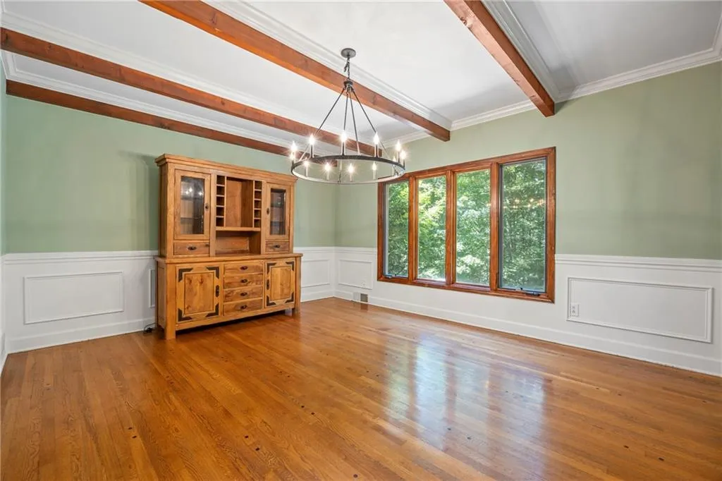 Unfurnished dining area with light wood finished floors, a chandelier, beam ceiling, ornamental molding, and wainscoting