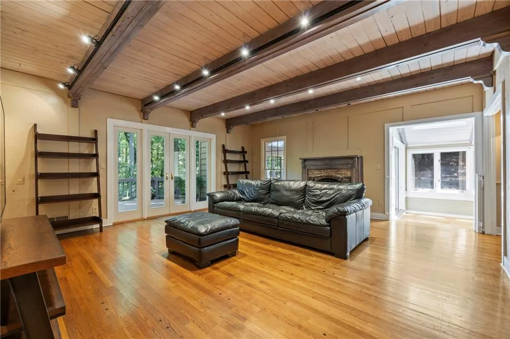 Living room featuring french doors, light wood-type flooring, a fireplace, track lighting, and a wooden ceiling with exposed beams