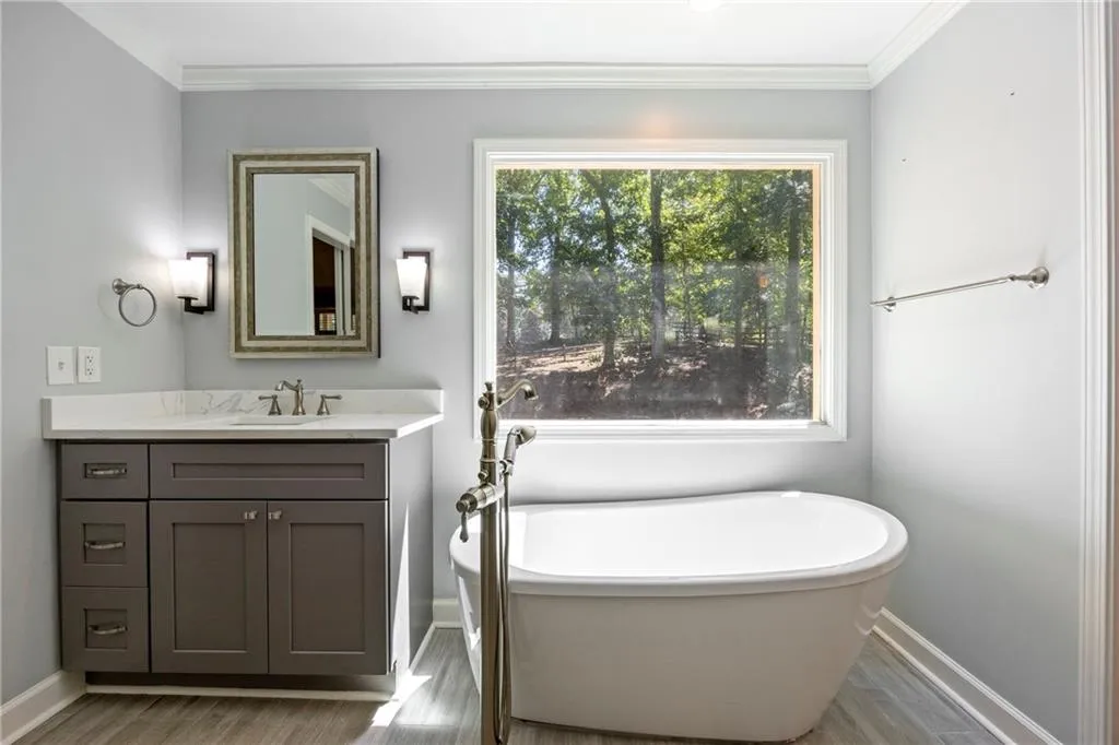 Full bathroom with a freestanding bath, vanity, light wood finished floors, and ornamental molding