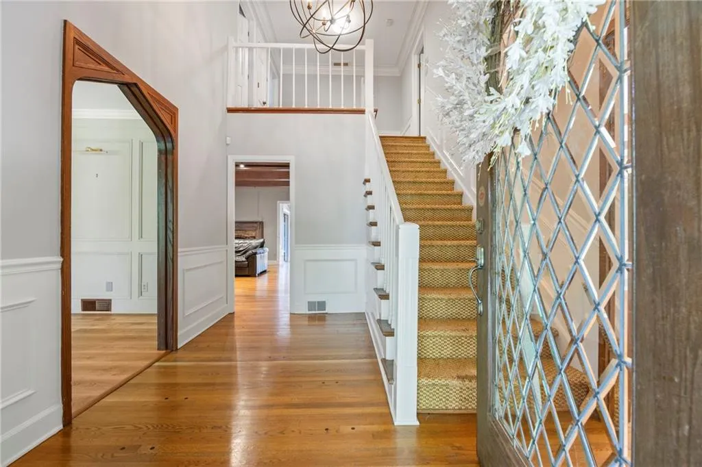Foyer featuring light wood-style flooring, a decorative wall, stairs, ornamental molding, and a wainscoted wall