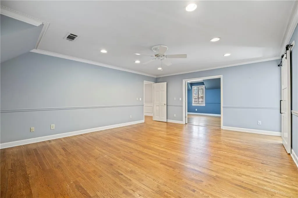 Spare room with a barn door, ornamental molding, recessed lighting, light wood-style floors, and a ceiling fan