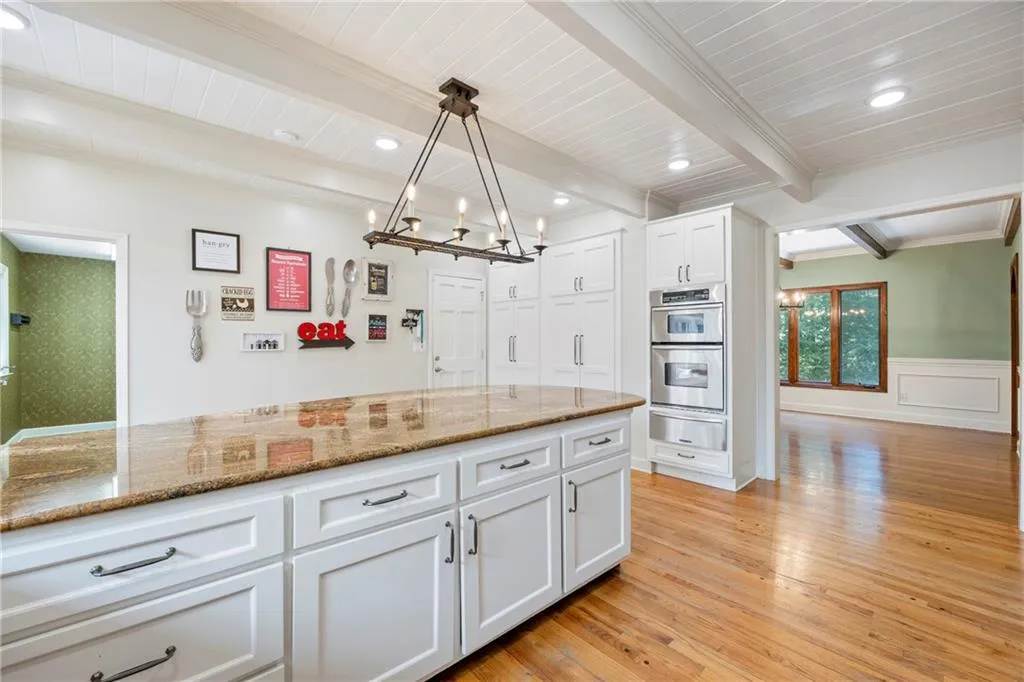 Kitchen featuring light wood-type flooring, dark stone countertops, pendant lighting, beam ceiling, and white cabinetry