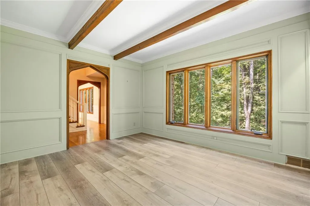 Empty room with arched walkways, light wood-style flooring, a decorative wall, ornamental molding, and beam ceiling