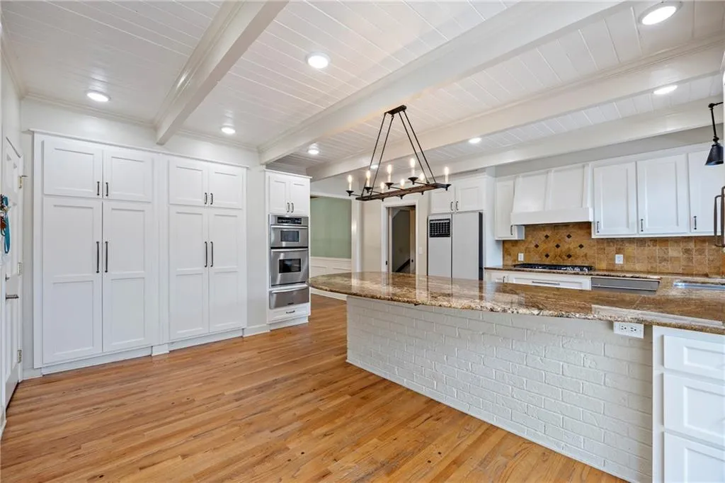 Kitchen with white cabinetry, a peninsula, light wood finished floors, decorative backsplash, and beamed ceiling