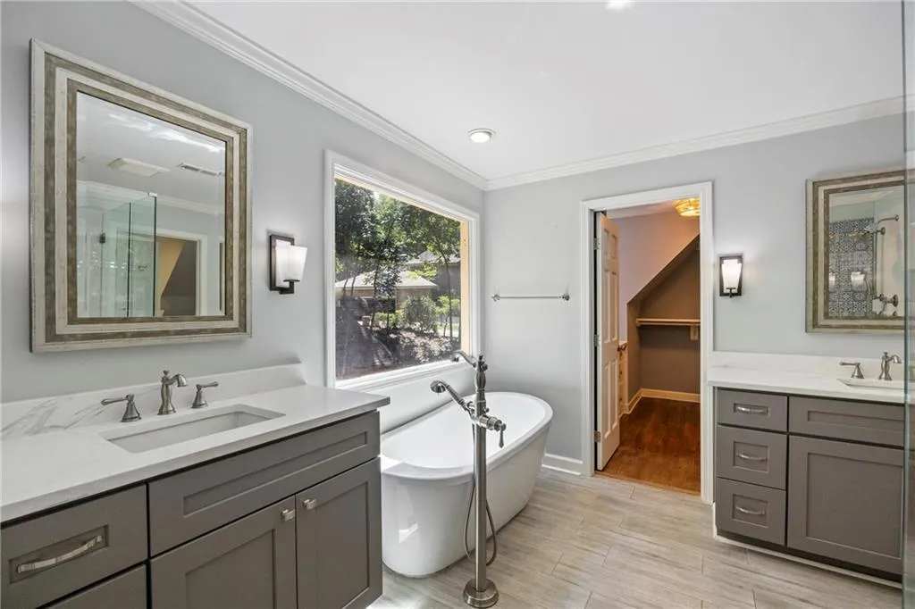 Bathroom featuring a freestanding bath, crown molding, two vanities, light wood-style floors, and a spacious closet