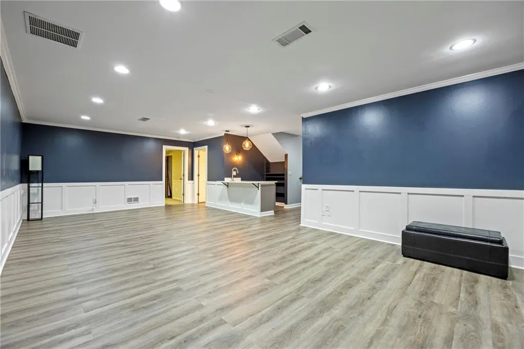 Unfurnished living room with ornamental molding, light wood-style flooring, a decorative wall, recessed lighting, and wainscoting