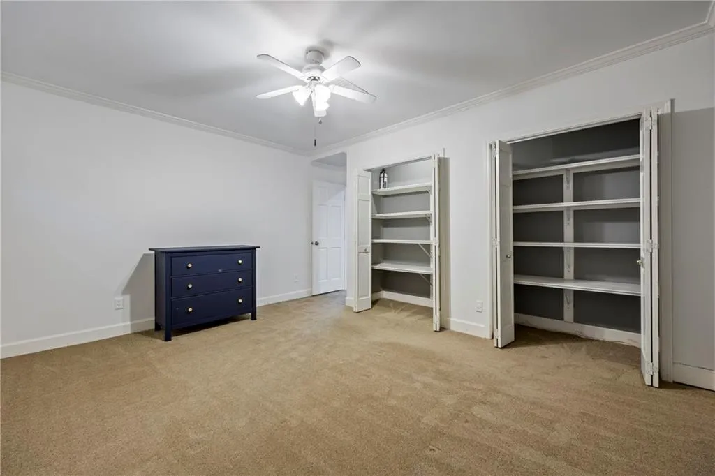 Unfurnished bedroom with crown molding, light colored carpet, two closets, and ceiling fan