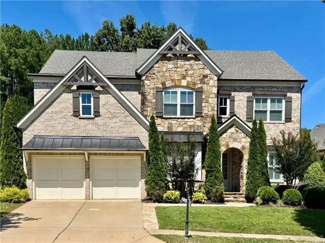 Brick and stone facade, gabled rooflines, dark window shutters, arched entry, and two-car garage