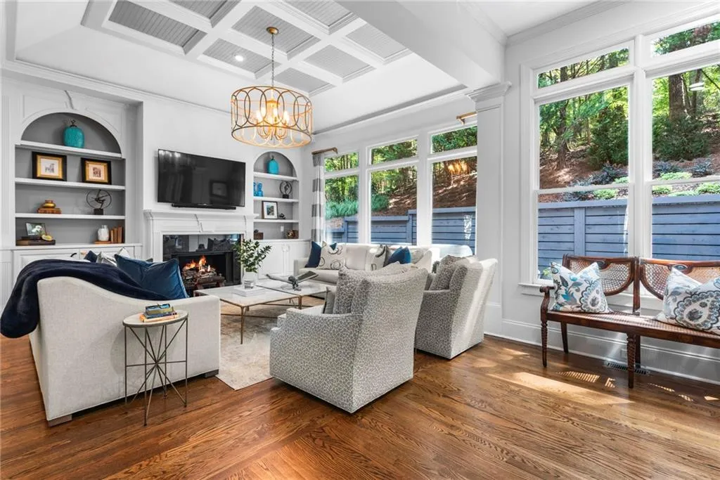 Family room with a beautiful view of the back patio area, featuring plenty of natural light with a wall of windows, coffered ceiling, fireplace, built-ins and designer chandelier Family room with a beautiful view of the back patio area, featuring plenty of natural light with a wall of windows, coffered ceiling, fireplace, built-ins and designer chandelier