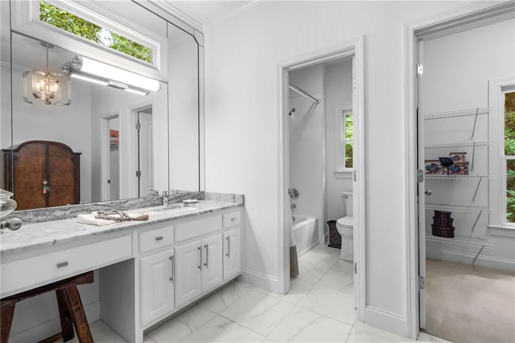 Guest Bathroom featuring vanity & makeup area, tub/shower combination, light marble finish flooring, crown molding, and spacious walk-in closet Guest Bathroom featuring vanity & makeup area, tub/shower combination, light marble finish flooring, crown molding, and spacious walk-in closet